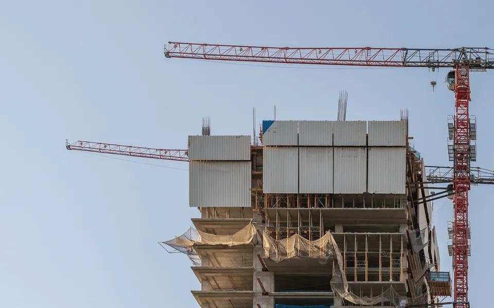 Puncak gedung beton bertingkat yang sedang dibangun dengan kren menara merah di langit biru